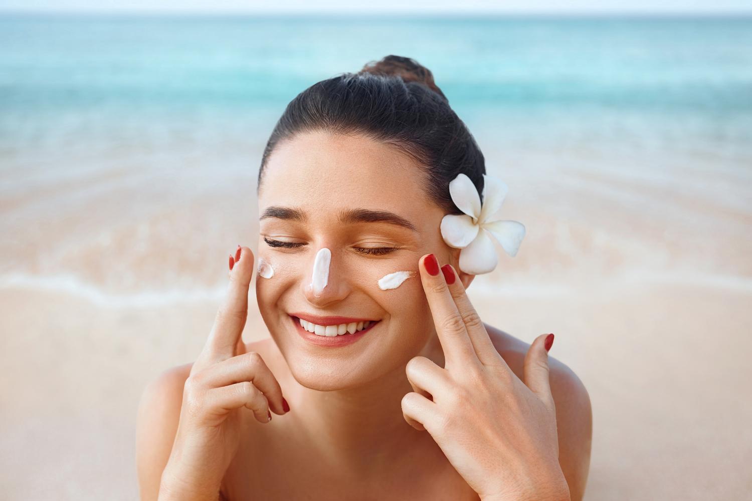 Frau liegt am Strand hat eine Blume im Haar und cremt sich mit Sonnencreme ein Hypogen Care